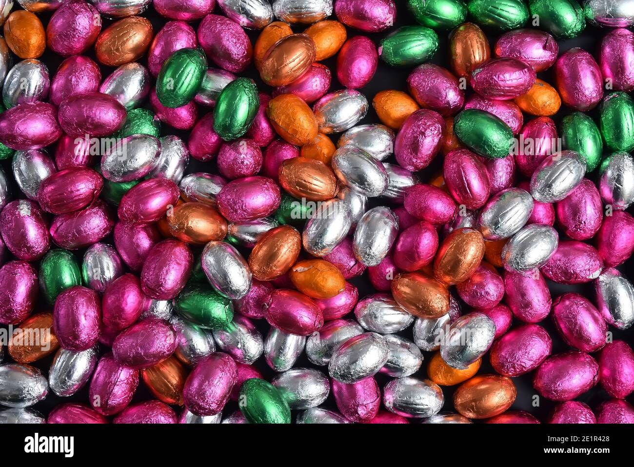 Pink, green, orange, silver and bronze foil wrapped chocolate easter eggs, against a black background. Stock Photo