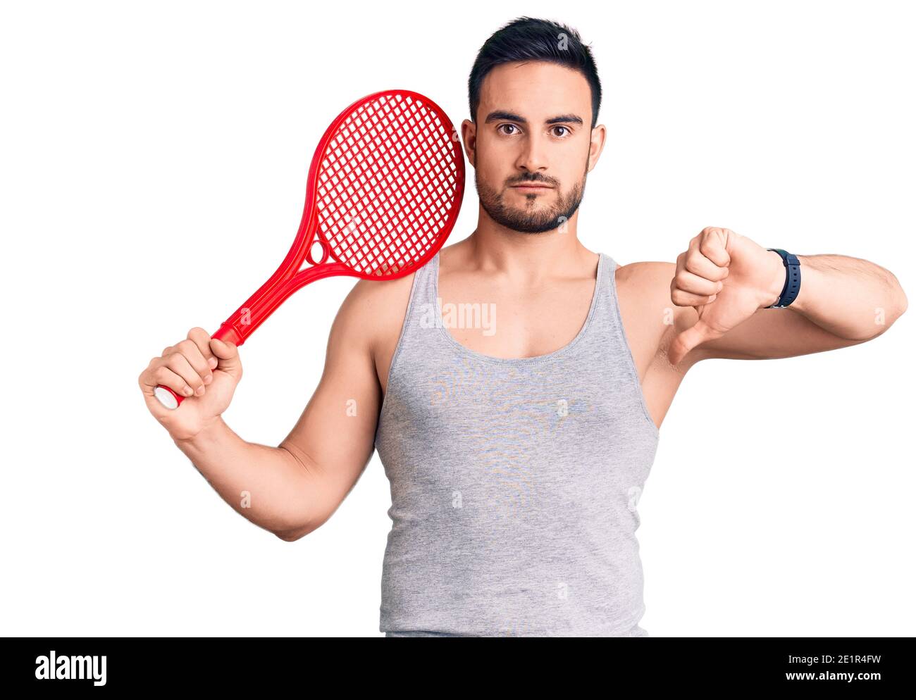 Young handsome man holding tennis racket with angry face, negative sign ...