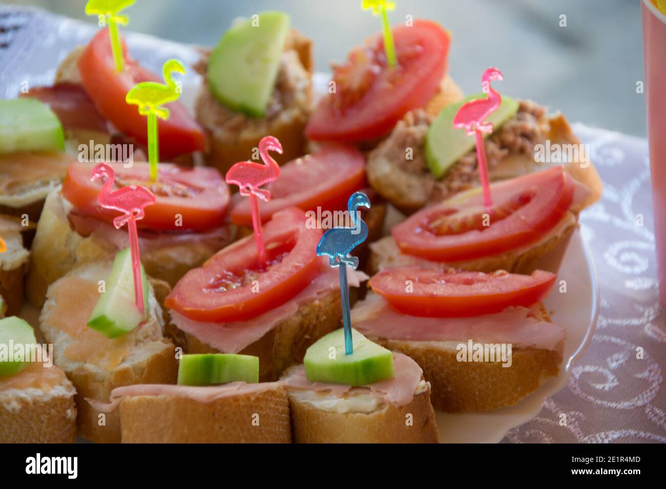 Healthy sandwiches with ham, tomato and cucumbers on a plate, decorated with plastic sticks with colorful flamingos, party concepts, appetizers for ce Stock Photo