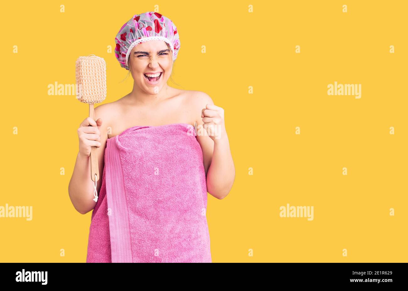 Young caucasian woman wearing shower cap and towel holding sponge