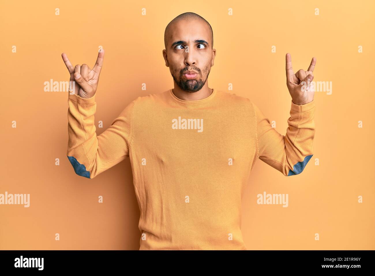 Squinting Rocks Hispanic adult man doing rock gesture over yellow background making ...