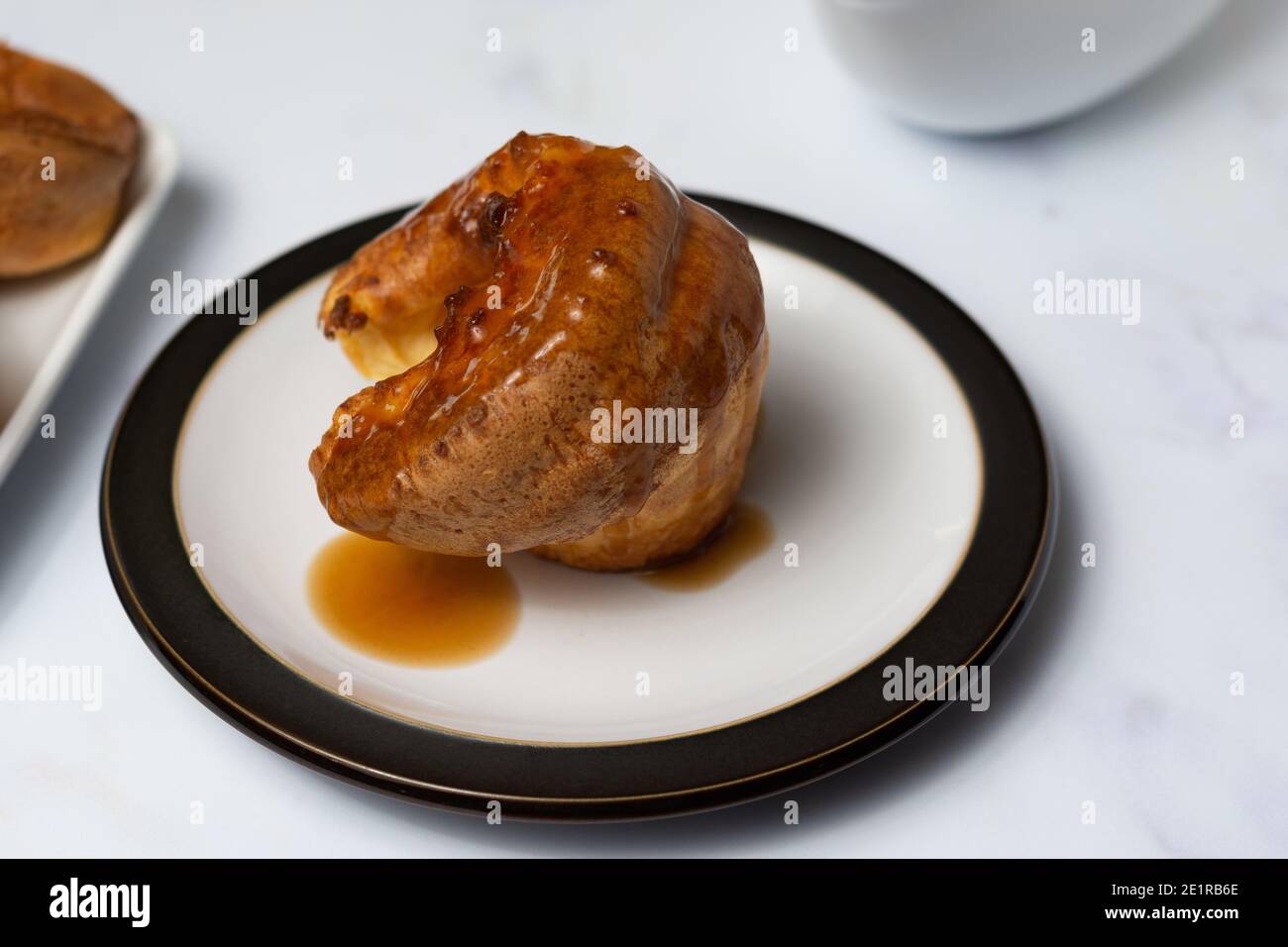 A single Yorkshire pudding covered in gravy sitting on a black rimmed plate on a white background Stock Photo
