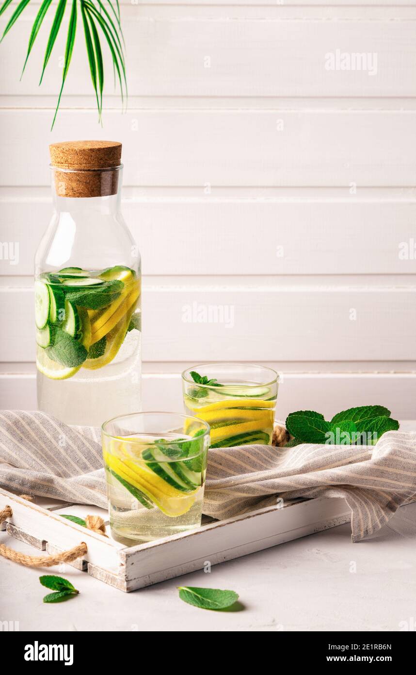 Sassy water for detox infused with lemon, cucumber and mint in glasses at white wooden tray. Healthy lifestyle concept. Space for text. Stock Photo