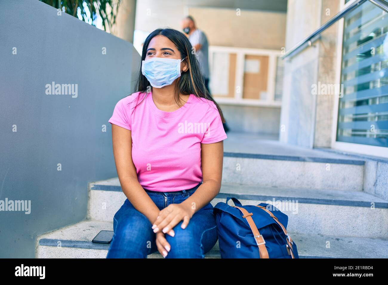 Young latin student girl wearing medical mask sitting on the stairs at ...