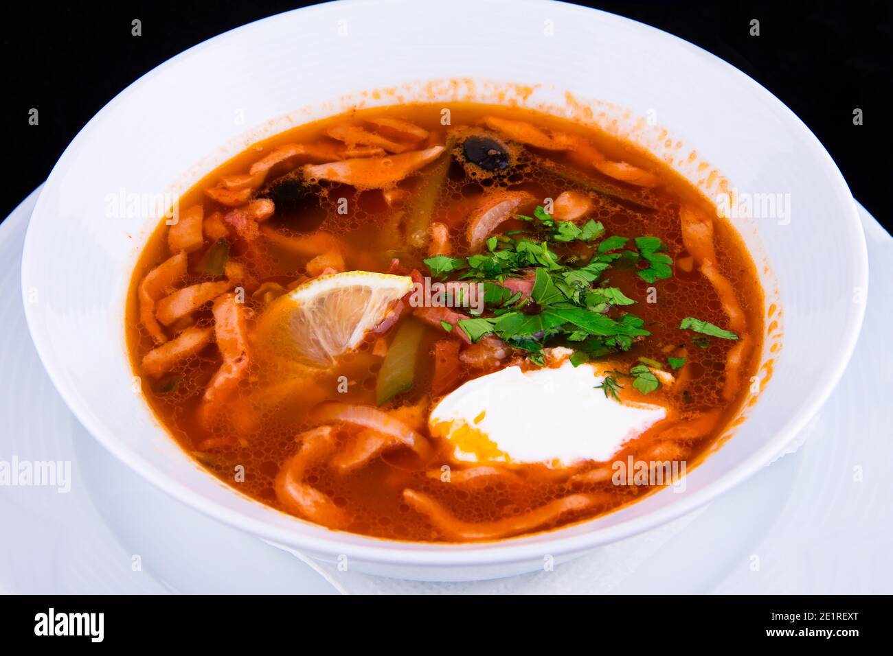 Traditional Russian soup Solyanka cooked with meat, sausages, salted cucumbers and olives sprinkled with herbs and seasoned with sour cream. Stock Photo