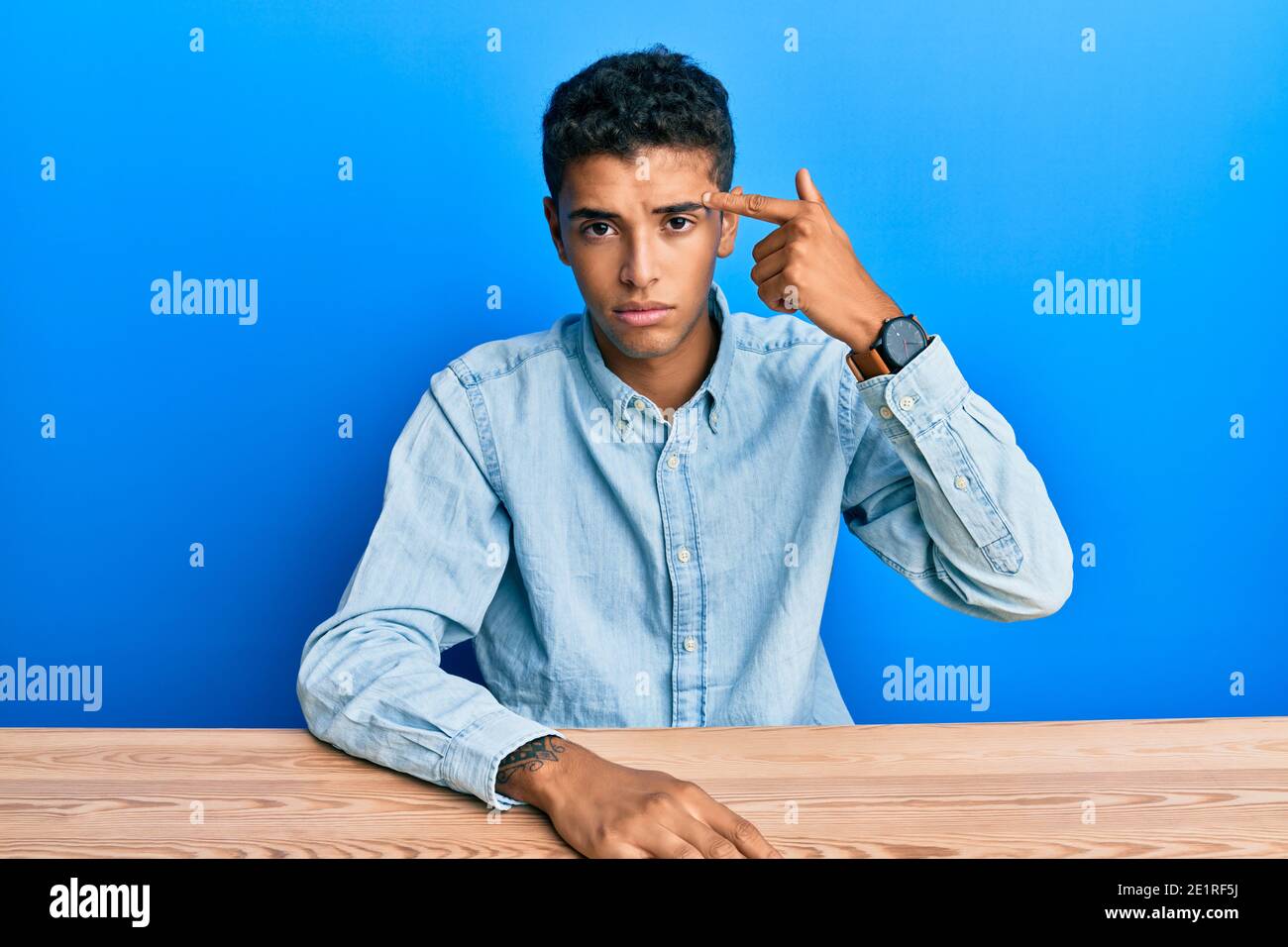 Young handsome african american man wearing casual clothes sitting on the table pointing unhappy to pimple on forehead, ugly infection of blackhead. a Stock Photo