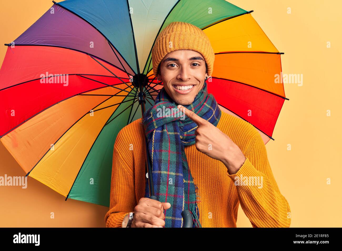 Young african amercian man holding colorful umbrella smiling happy pointing with hand and finger