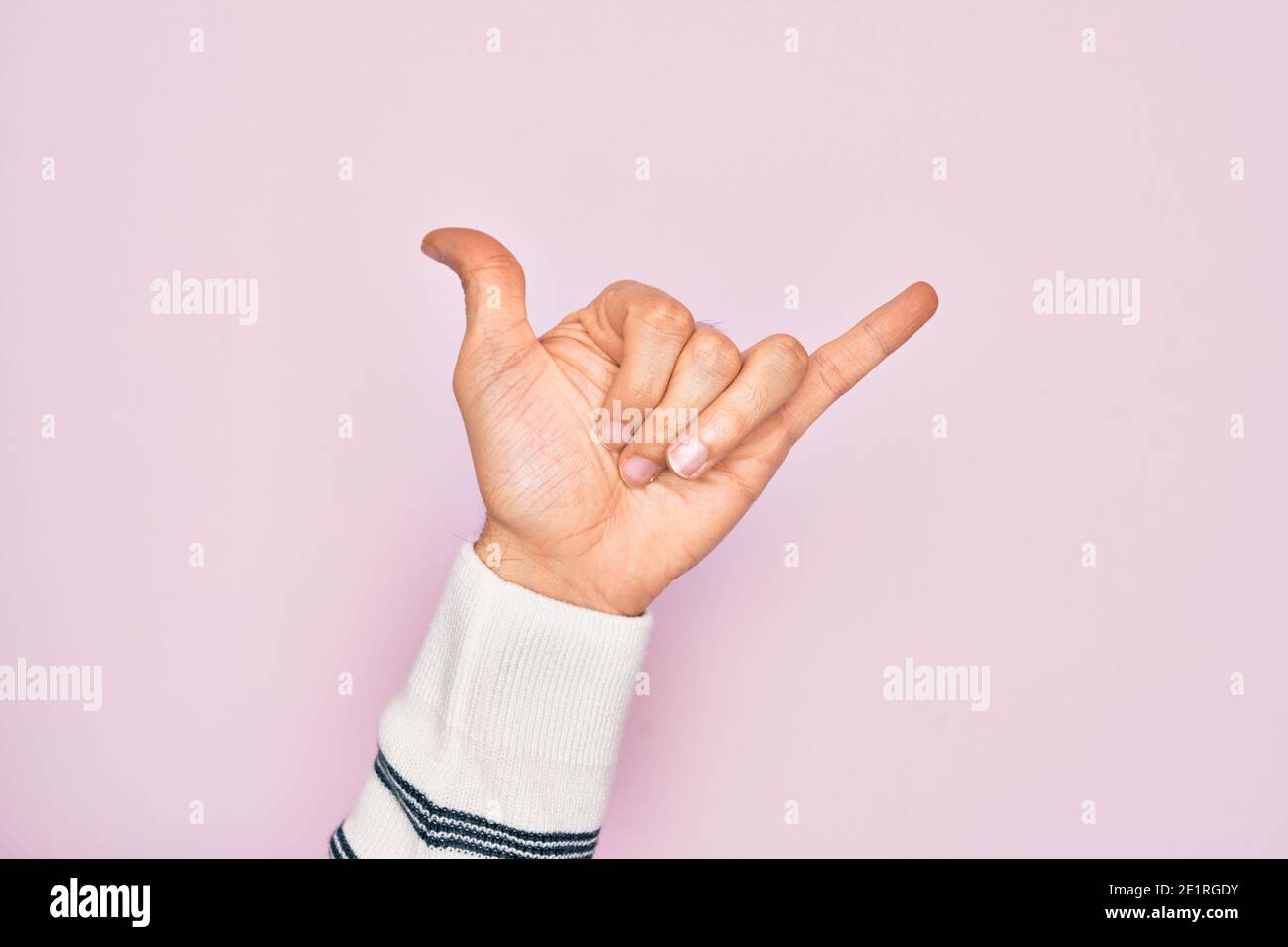 Hand of caucasian young man showing fingers over isolated pink background gesturing Hawaiian shaka greeting gesture, telephone and communication symbo Stock Photo
