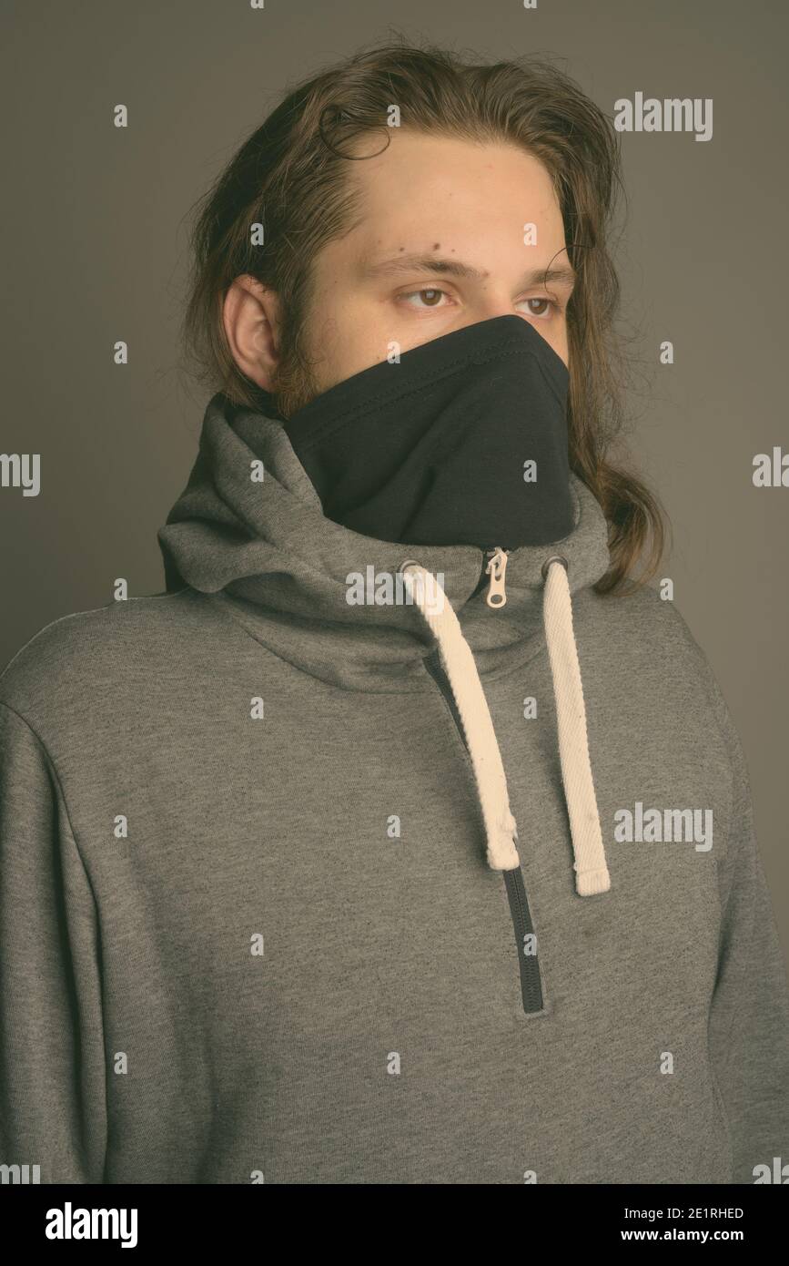 Young bearded man wearing gray hoodie and mask against gray background Stock Photo