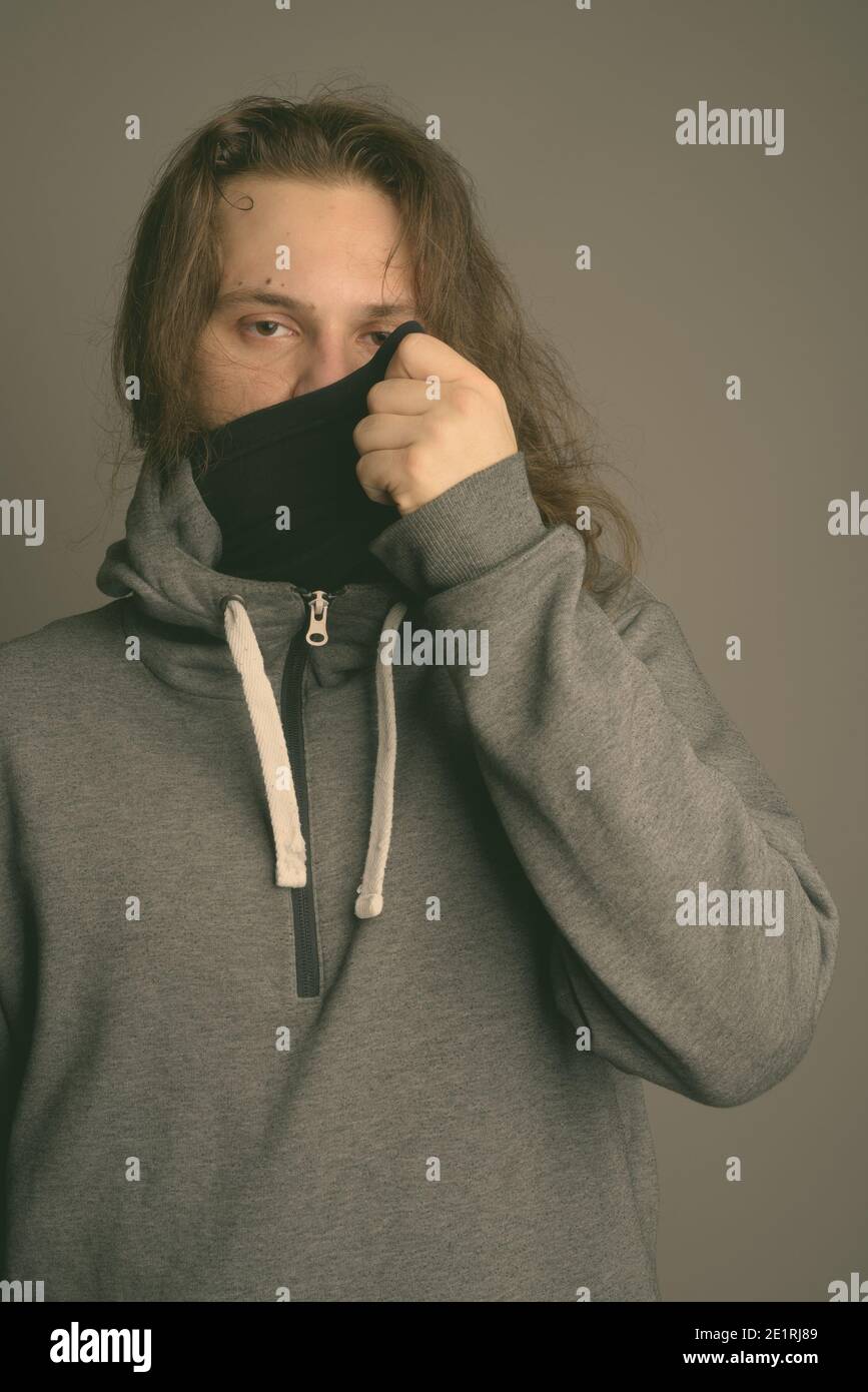 Young bearded man wearing gray hoodie and mask against gray background Stock Photo