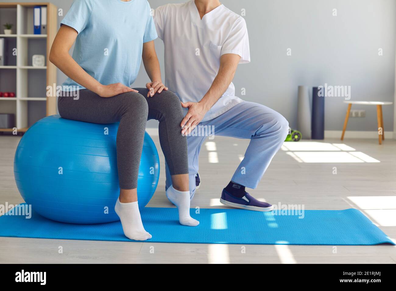 Woman doing exercise on fit ball with professional physiotherapist or chiropractor helping her Stock Photo