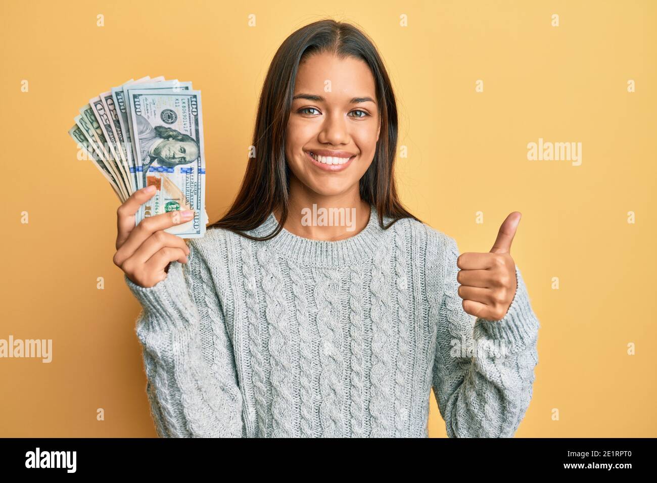 Beautiful hispanic woman holding dollars smiling happy and positive ...