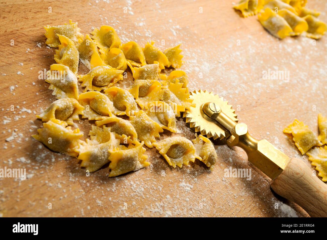 Ravioli del plin, typical pasta from Langhe, Piedmont, Italy - agnolotti with wheel knife on wooden cutting board Stock Photo