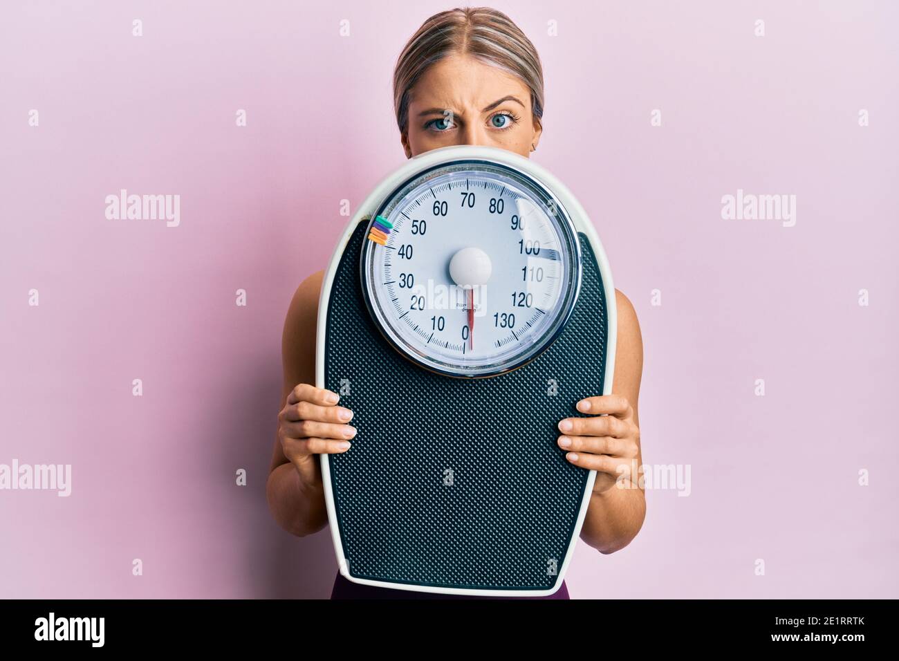 https://c8.alamy.com/comp/2E1RRTK/beautiful-blonde-woman-holding-weight-machine-to-balance-weight-loss-skeptic-and-nervous-frowning-upset-because-of-problem-negative-person-2E1RRTK.jpg