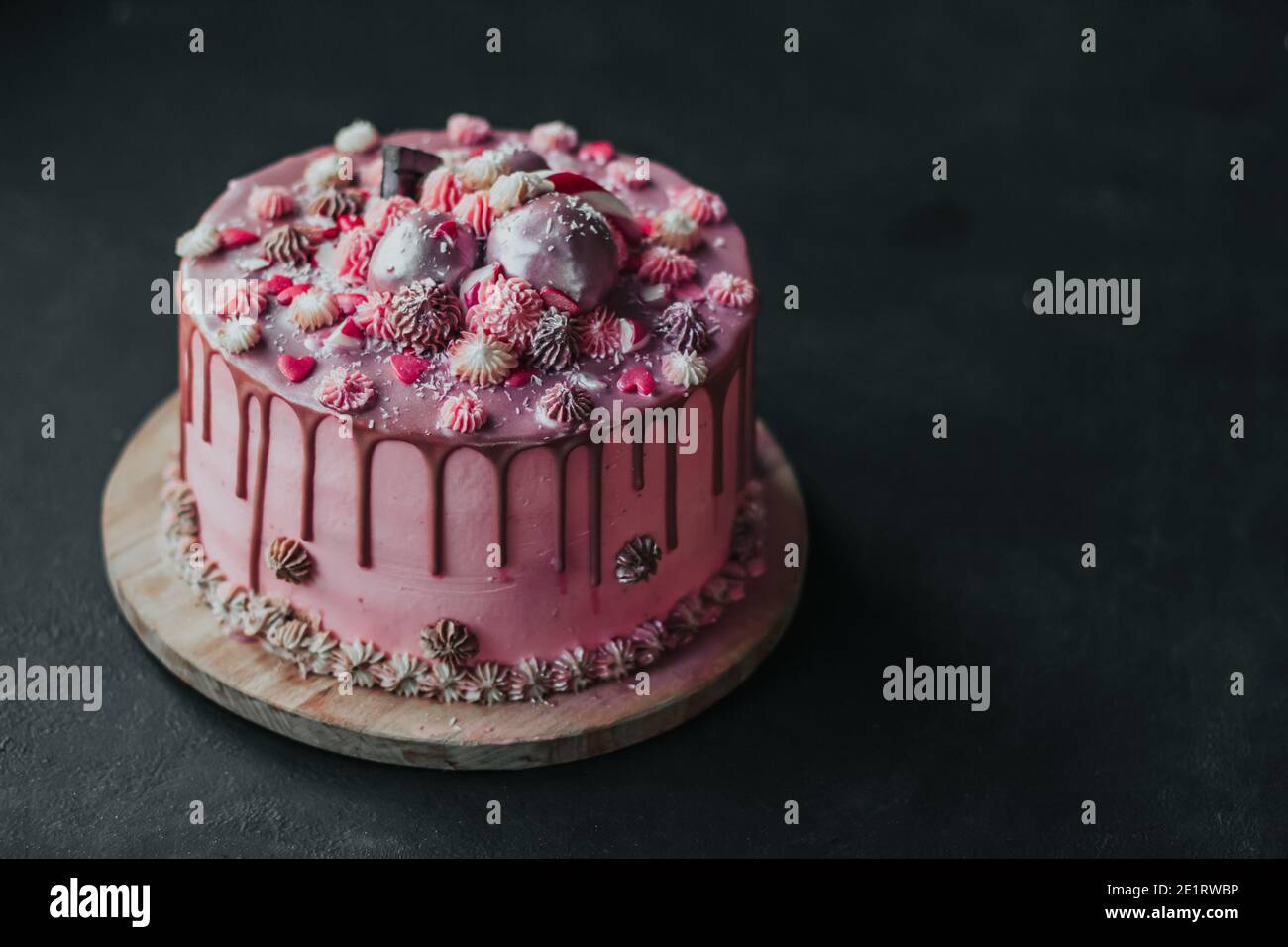 Birthday cake with pink cream and chocolate icing, sprinkled with hearts and sweets. Homemade cake copy space Stock Photo