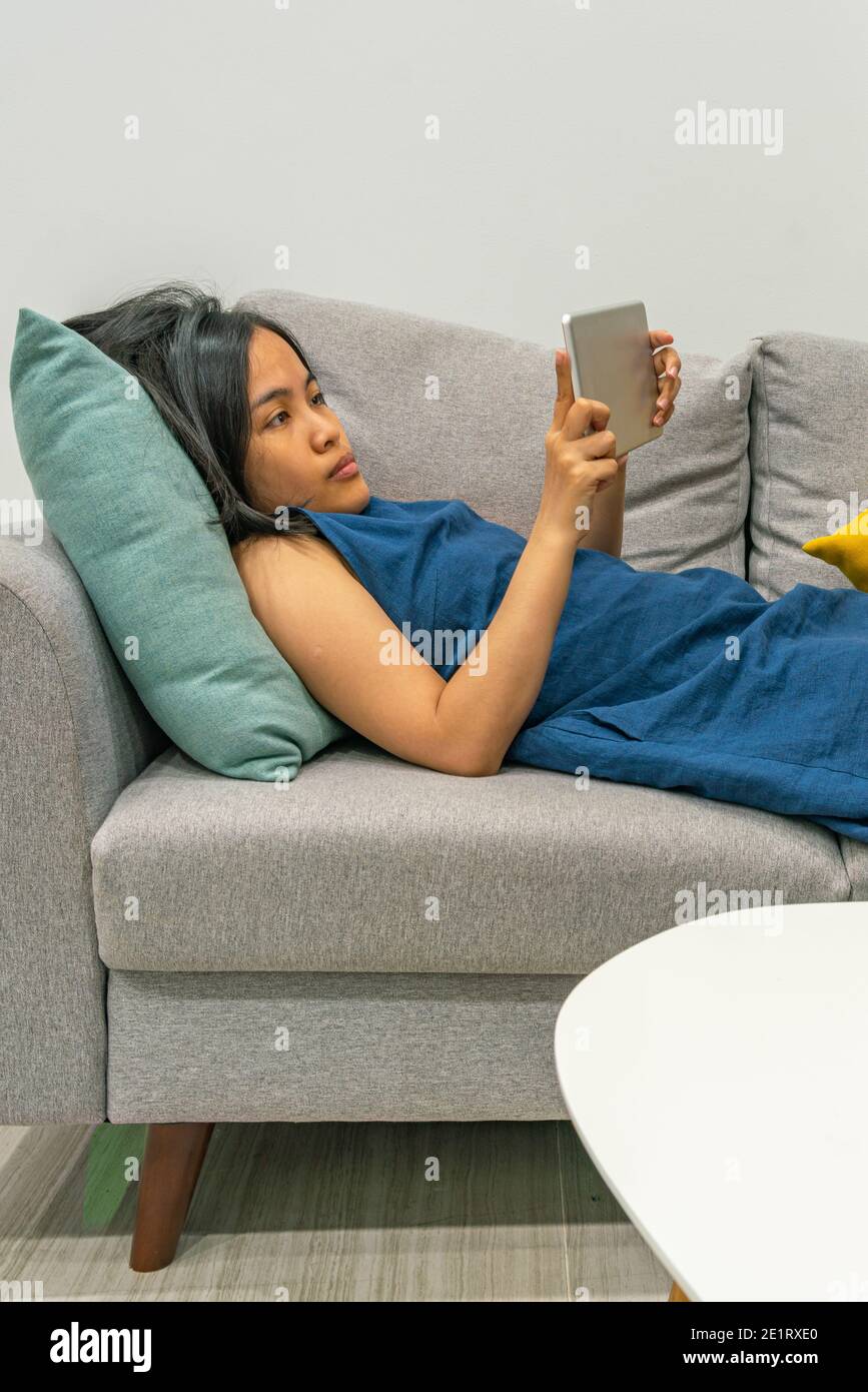 Vertical photo of Asian woman using tablet on the sofa Stock Photo - Alamy