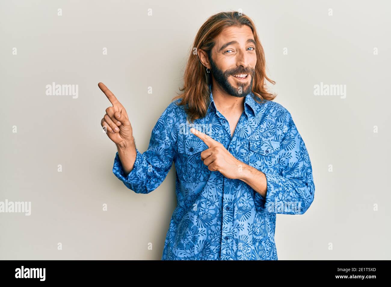 Attractive man with long hair and beard wearing 80s disco style shirt  smiling and looking at the camera pointing with two hands and fingers to  the sid Stock Photo - Alamy