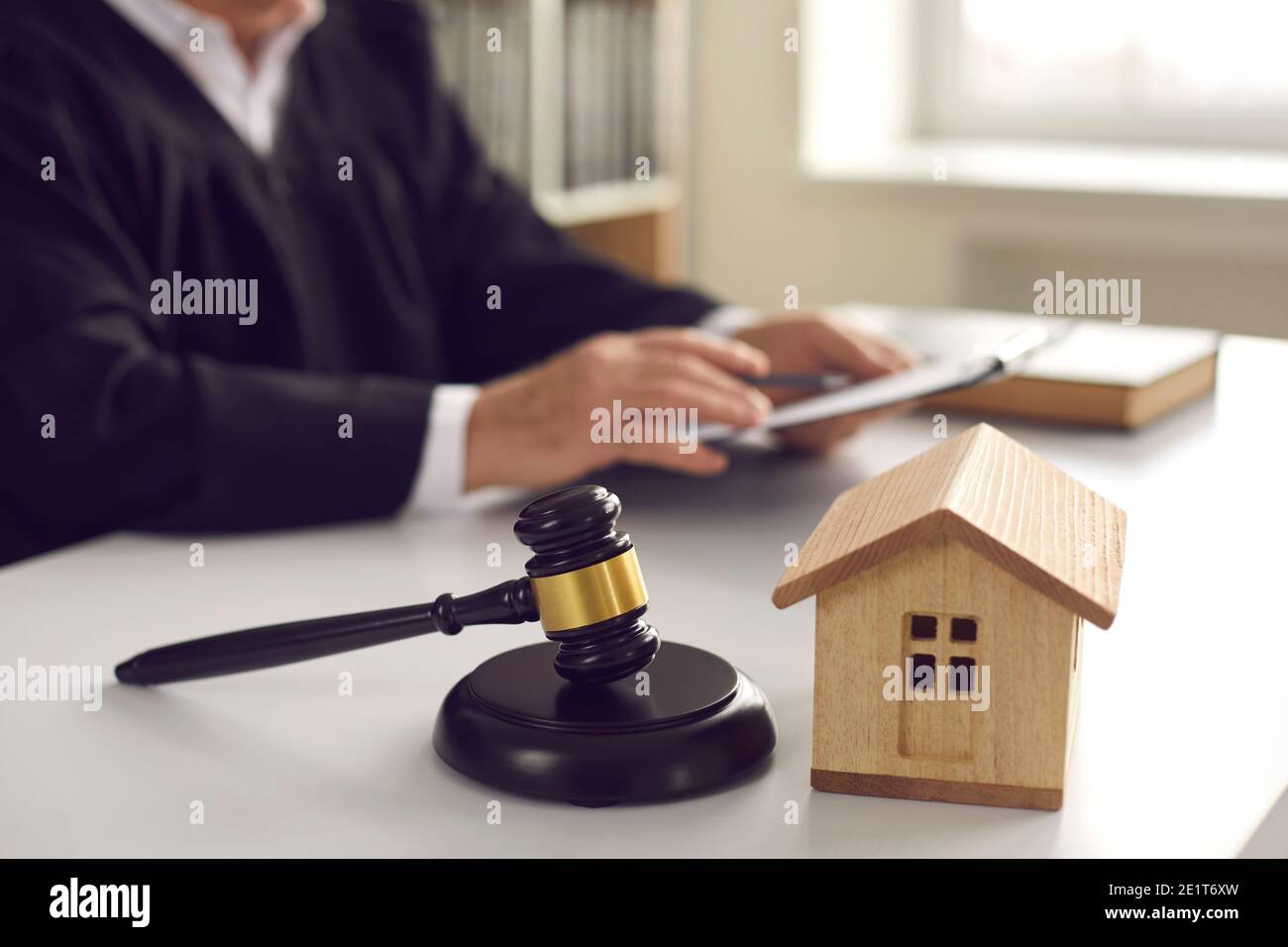 Gavel on sound block and toy house on judge's table in courtroom during court hearing Stock Photo