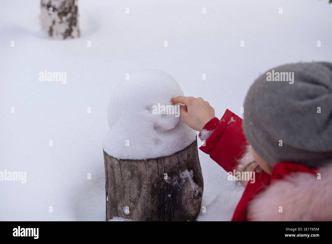 A girl in winter clothes draws a smiley face in the snow on a stump. The concept of winter fun Stock Photo
