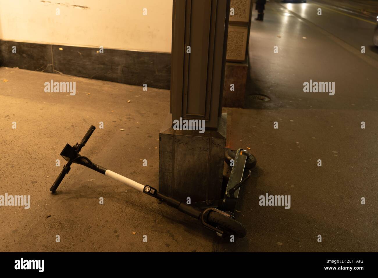 Electric scooter lying down on sidewalk in dark evening. Problem of share system rules. Zurich