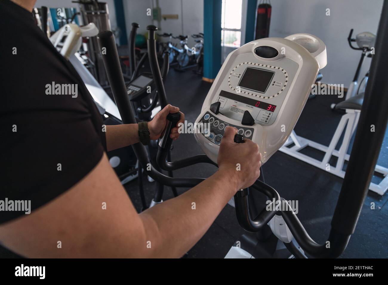 Unrecognizable man hands on elliptical trainer handrails in sport club. Cardio workout background, running on treadmill. Healthy lifestyle, guy traini Stock Photo