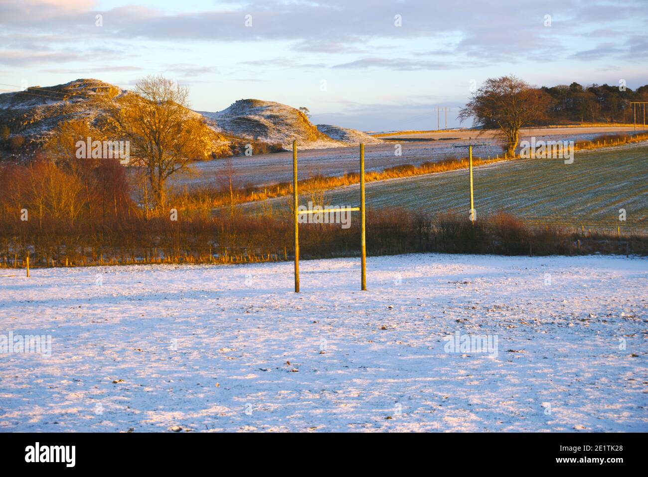 Rugby goalposts in a snowy field with trees, farmland and hills illuminated by a winter sunset, Berwickshire, Scottish Borders, Scotland, UK. Stock Photo