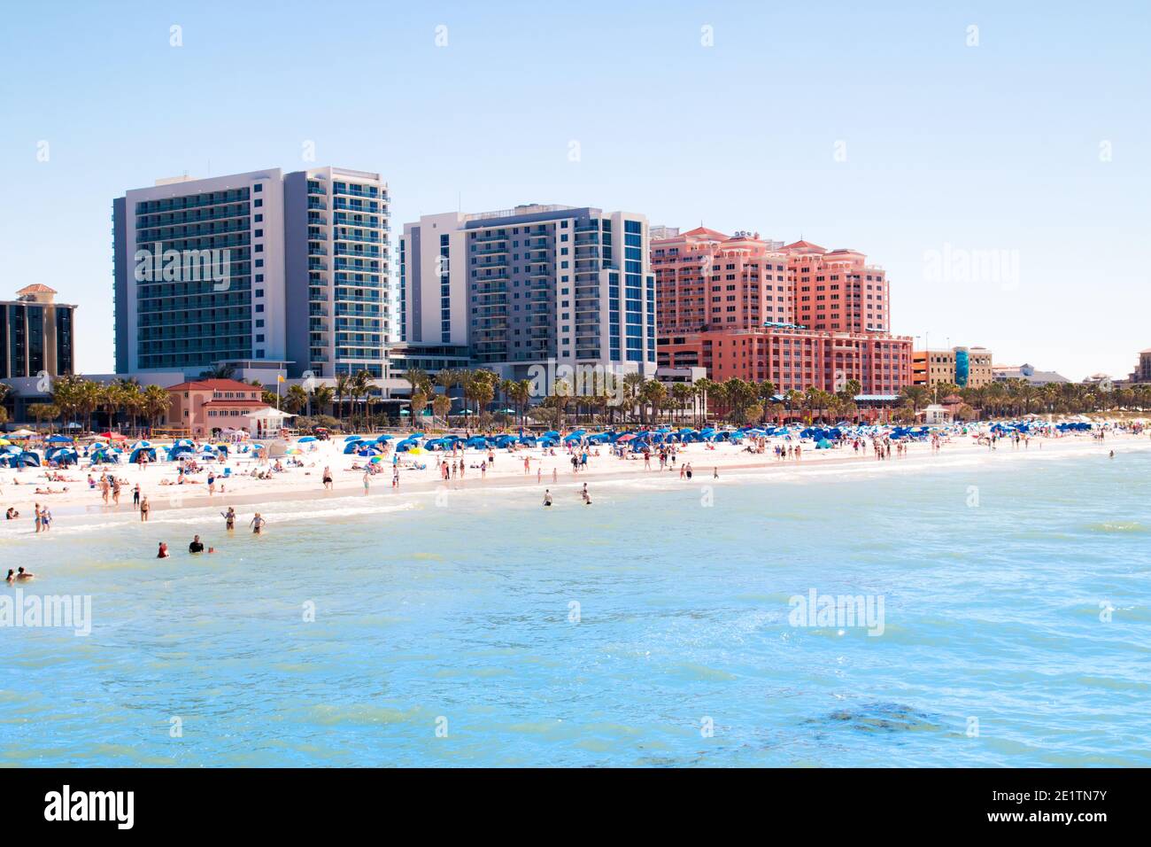 Tropical sandy beach vacation city Clearwater Beach in Florida, colourful beachfront hotel resorts buildings, sea and sunbathing tourists Stock Photo