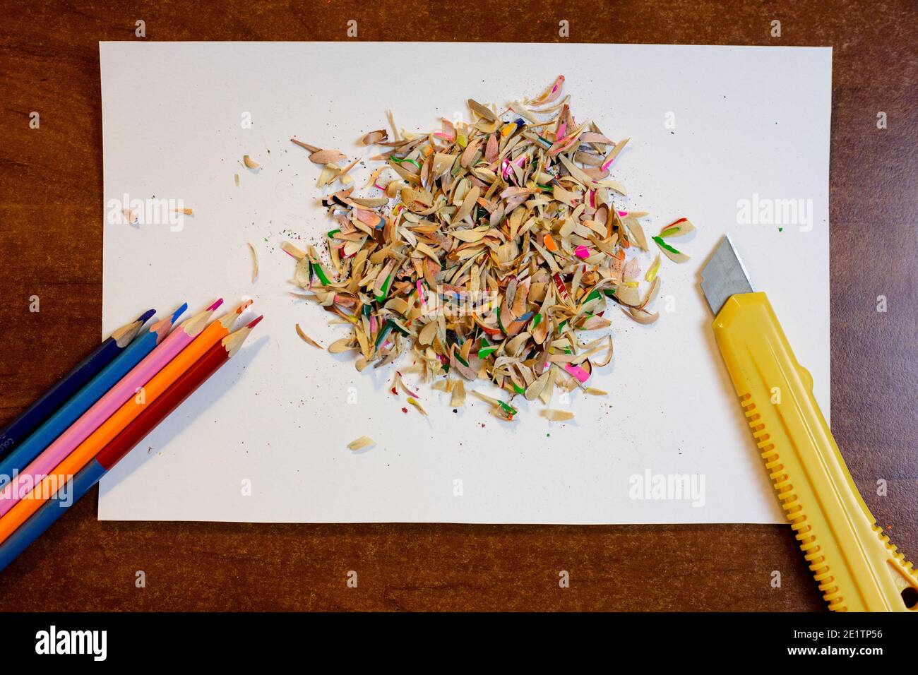 Colored pencils, shavings on a white background and a stationery knife