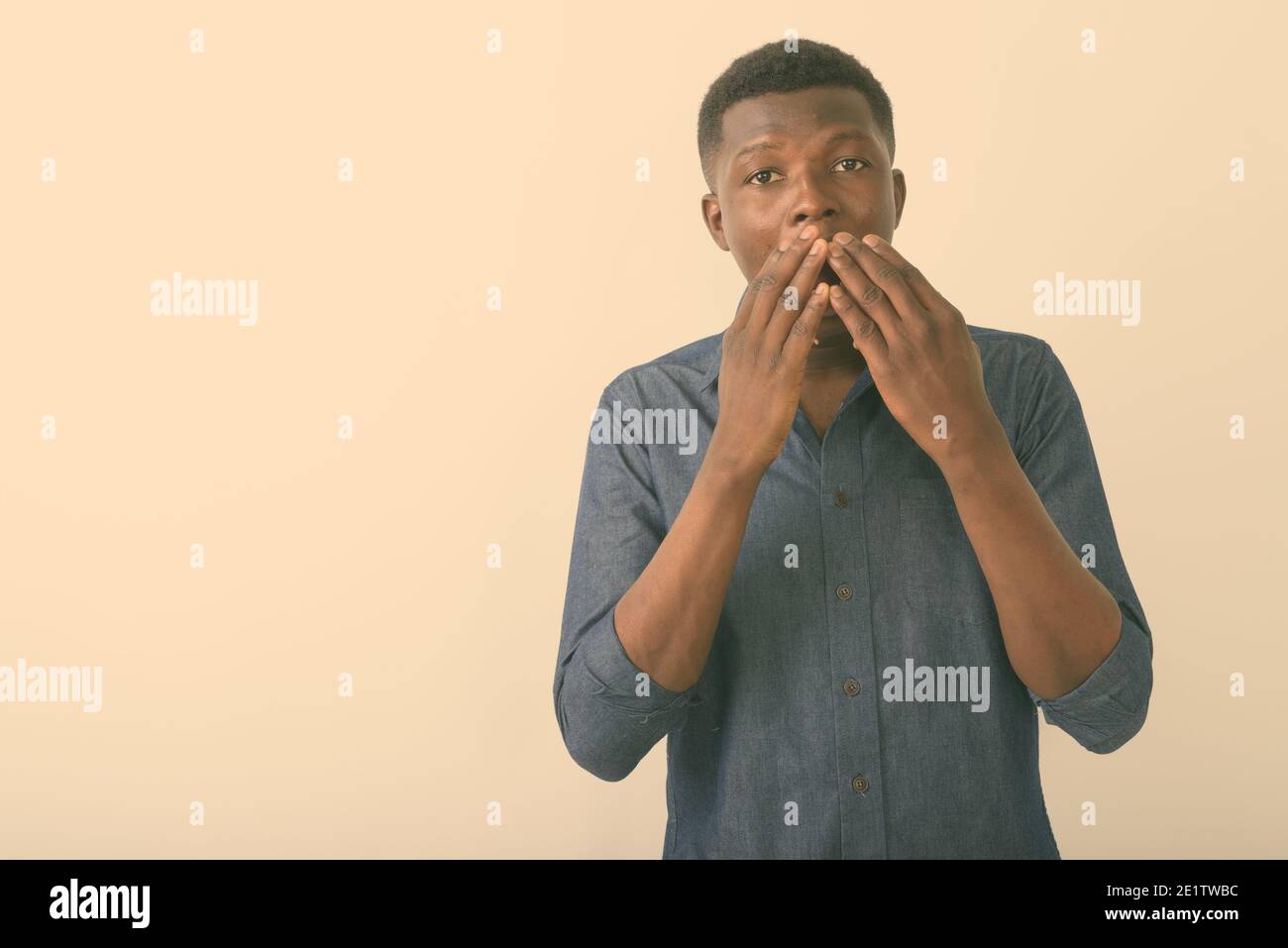 Studio shot of young black African man looking shocked while covering ...