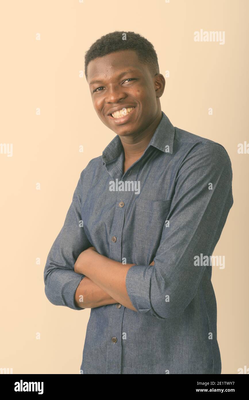 Studio shot of young happy black African man smiling with arms crossed ...
