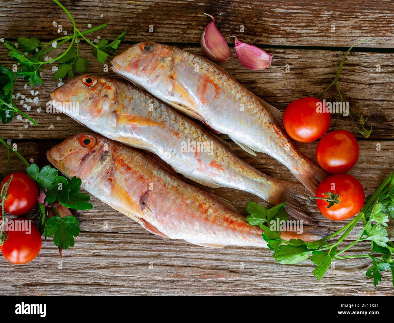 red mullet on an old wooden board background with typical ingredients of an Italian recipe 'triglie alla livornese' Stock Photo