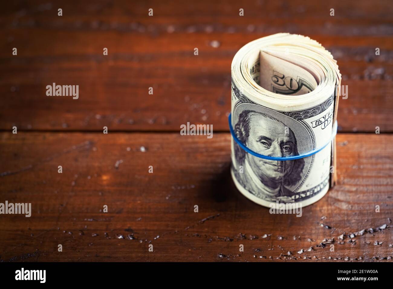 Roll of money with rubber on wooden table - one hundred US banknotes with president Franklin portrait. Cash of hundred dollar bills, paper currency ba Stock Photo