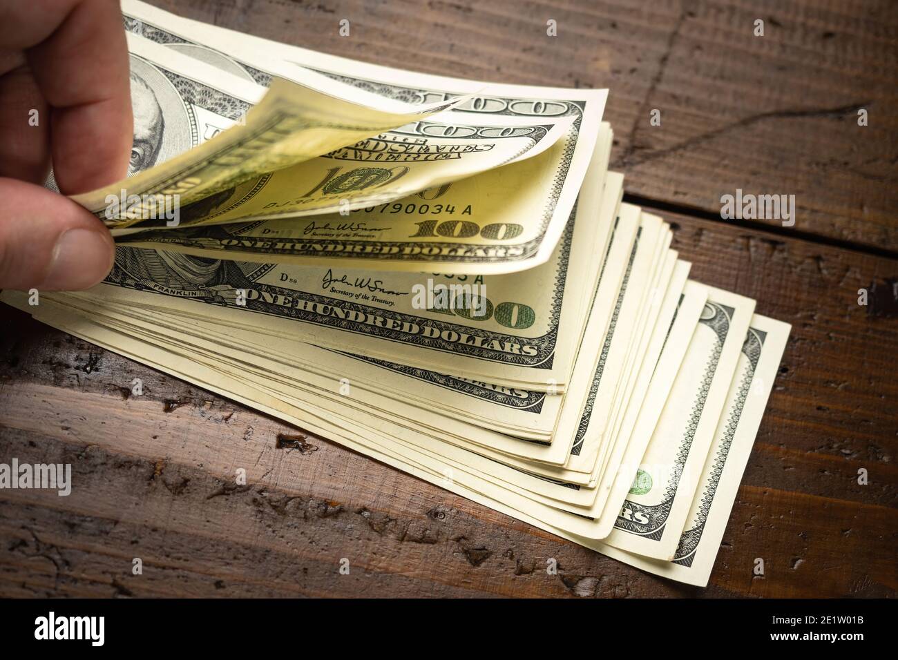 Hand counting pile of one hundred US banknotes on wooden table background. Cash of hundred dollar bills, paper money currency. Stock Photo