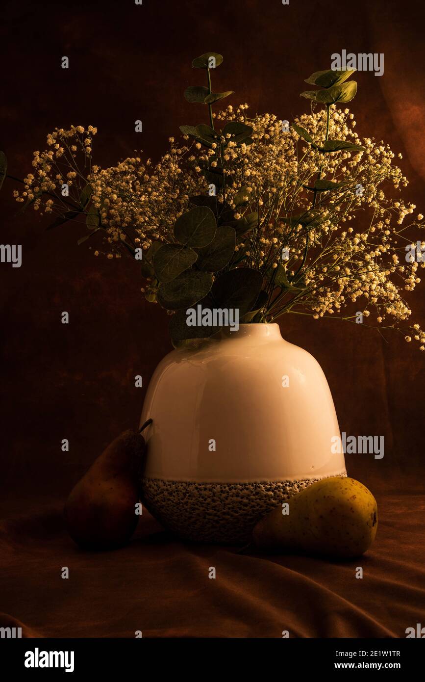 Soft white vase with 'baby's breath' flowers on a dark background,  Artificial fruit adds a nice accent. Stock Photo