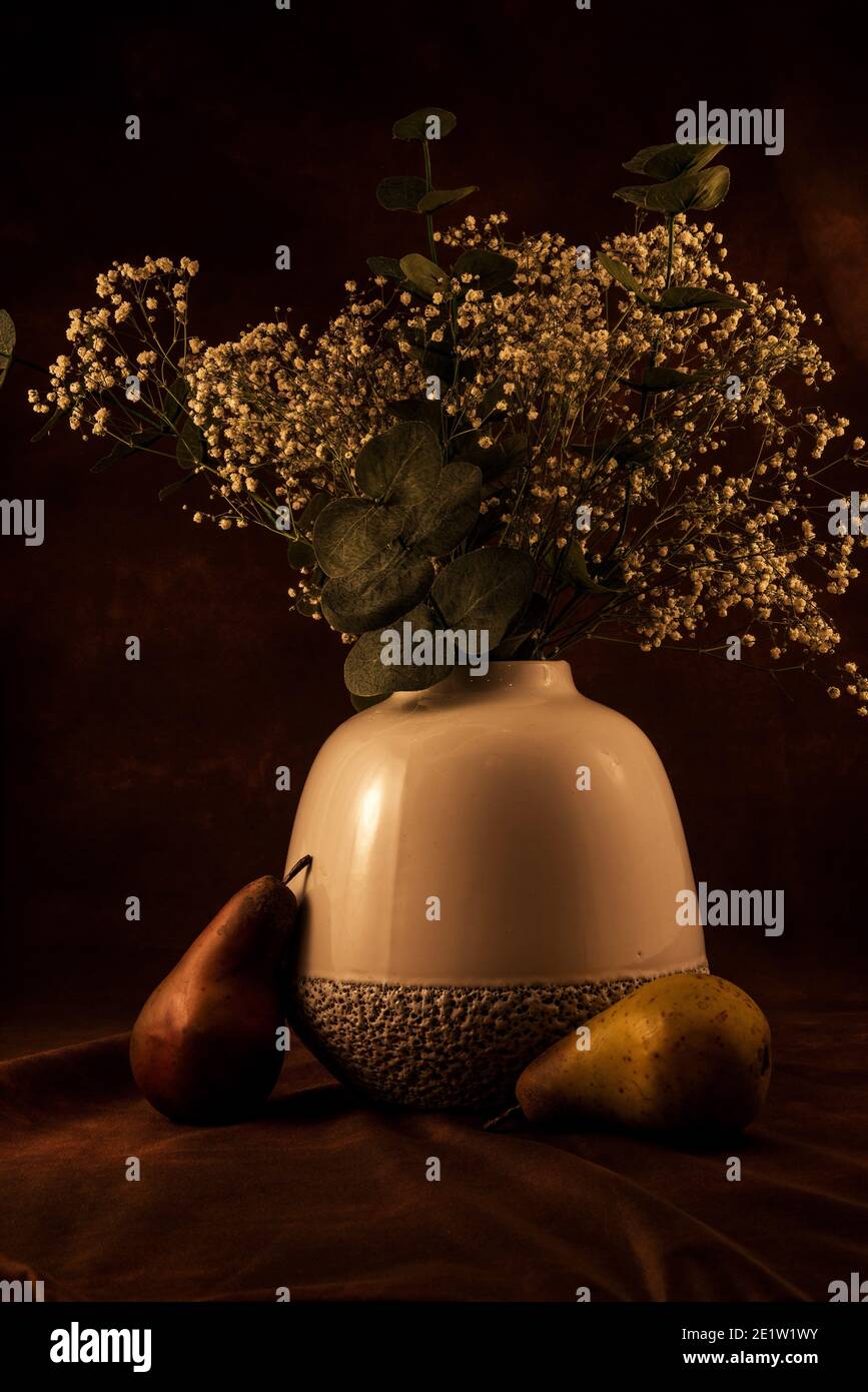 Soft white vase with 'baby's breath' flowers on a dark background,  Artificial fruit adds a nice accent. Stock Photo