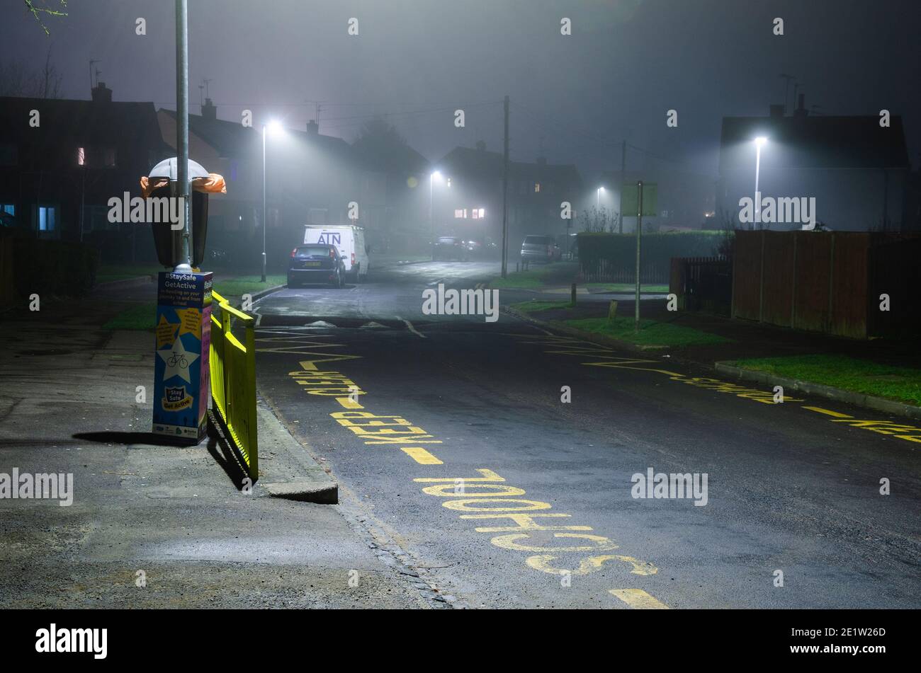 Nighttime shot of 'School Keep Clear' painted on a road in a residential area. Street lights look diffused in the fog. Stock Photo