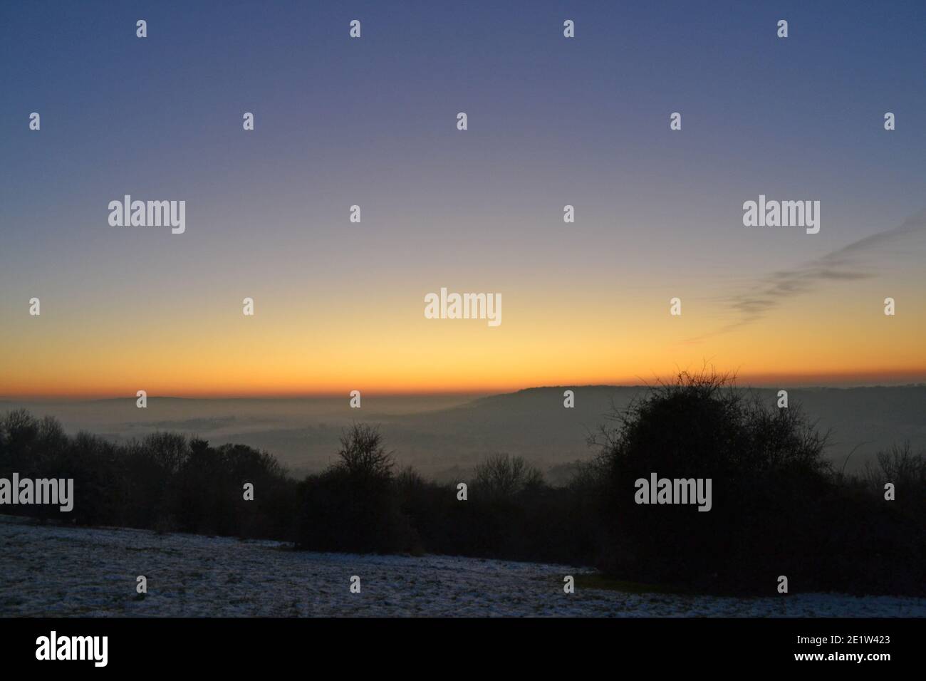Dramatic sunset in misty winter light in the North Downs, Fackenden Down, in Kent, near Sevenoaks, crisp, clear sky above huge orange glow, blue sky Stock Photo