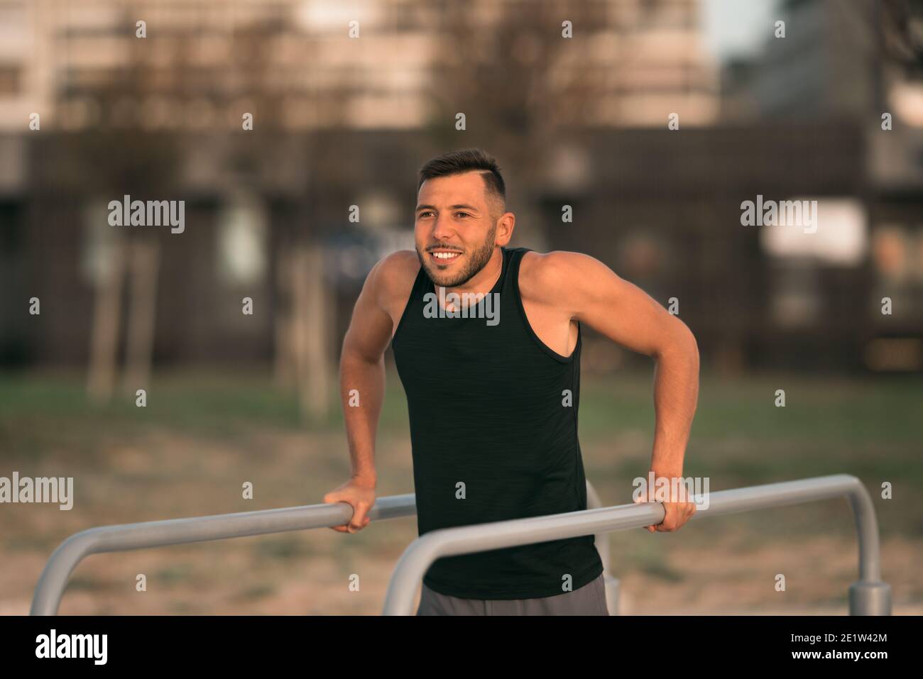 Young fit man doing triceps dips on parallel bars outdoors. Doing exercises on parallel bars Stock Photo