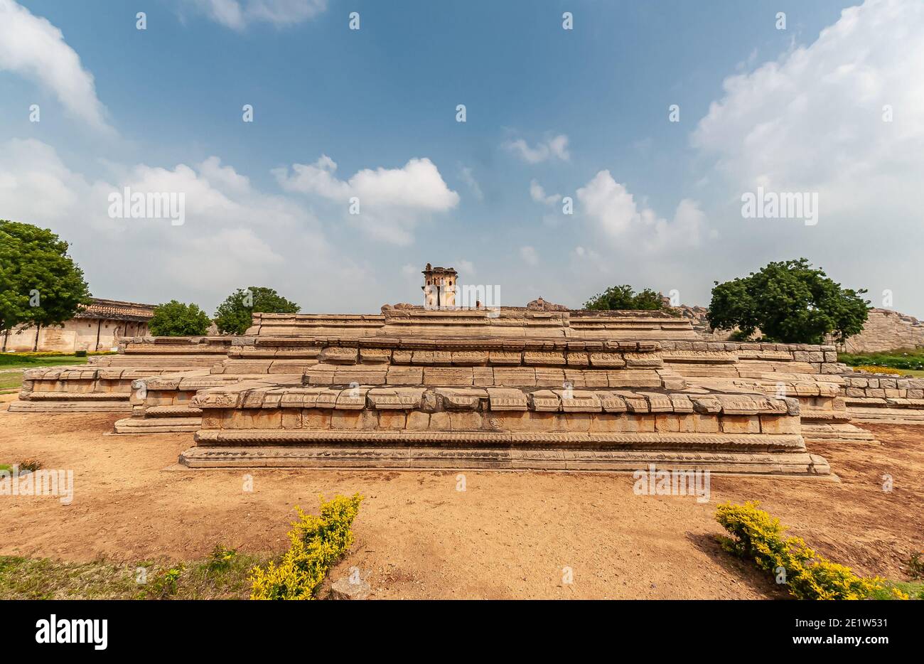 Hampi, Karnataka, India - November 5, 2013: Zanana Enclosure. Brown stone platform as remaining base of Queens Palace under blue cloudscape. Some gree Stock Photo