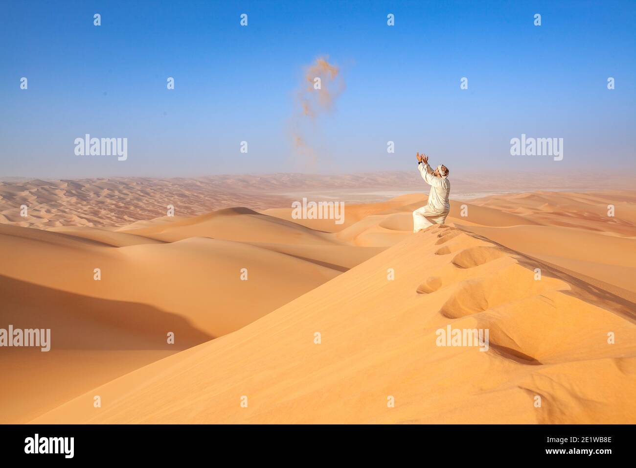 Man in traditional omani outfit throwing sand over a sand dune in the arabian desert Stock Photo