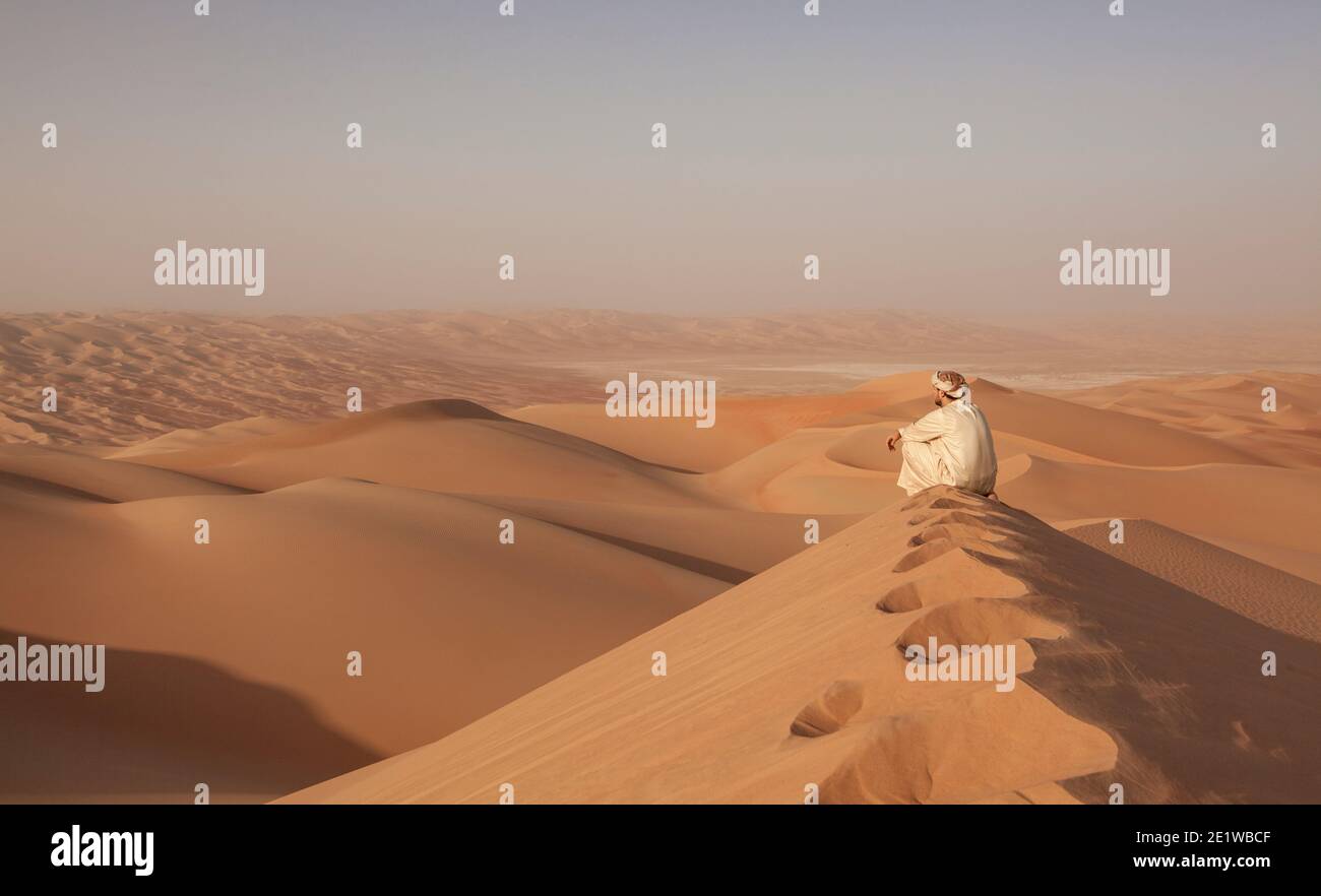 arab man in tradition outfit on a Dune in arabian Desert Stock Photo