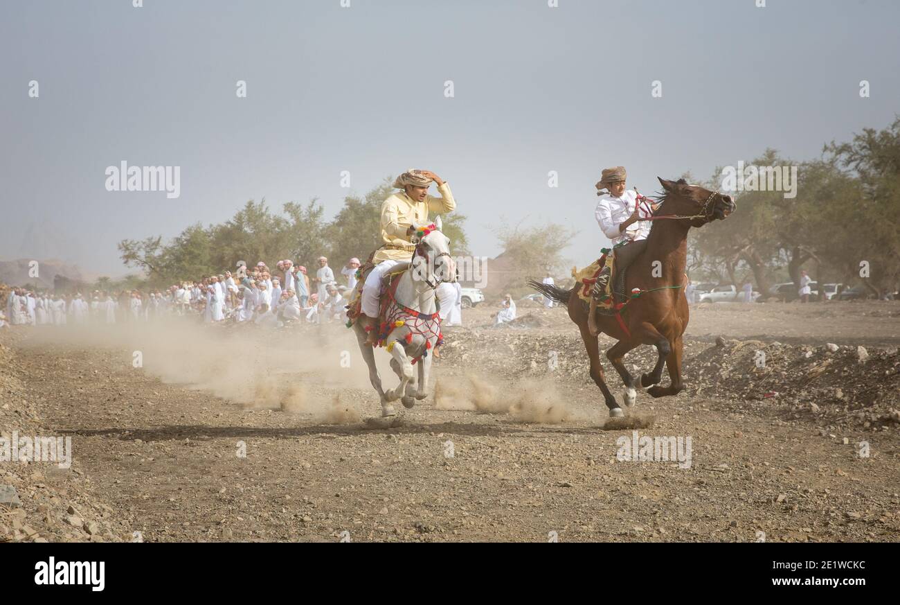 Khadal, Oman, April 7th, 2018: Men racing on horses to show their skill in a dusty countryside road Stock Photo