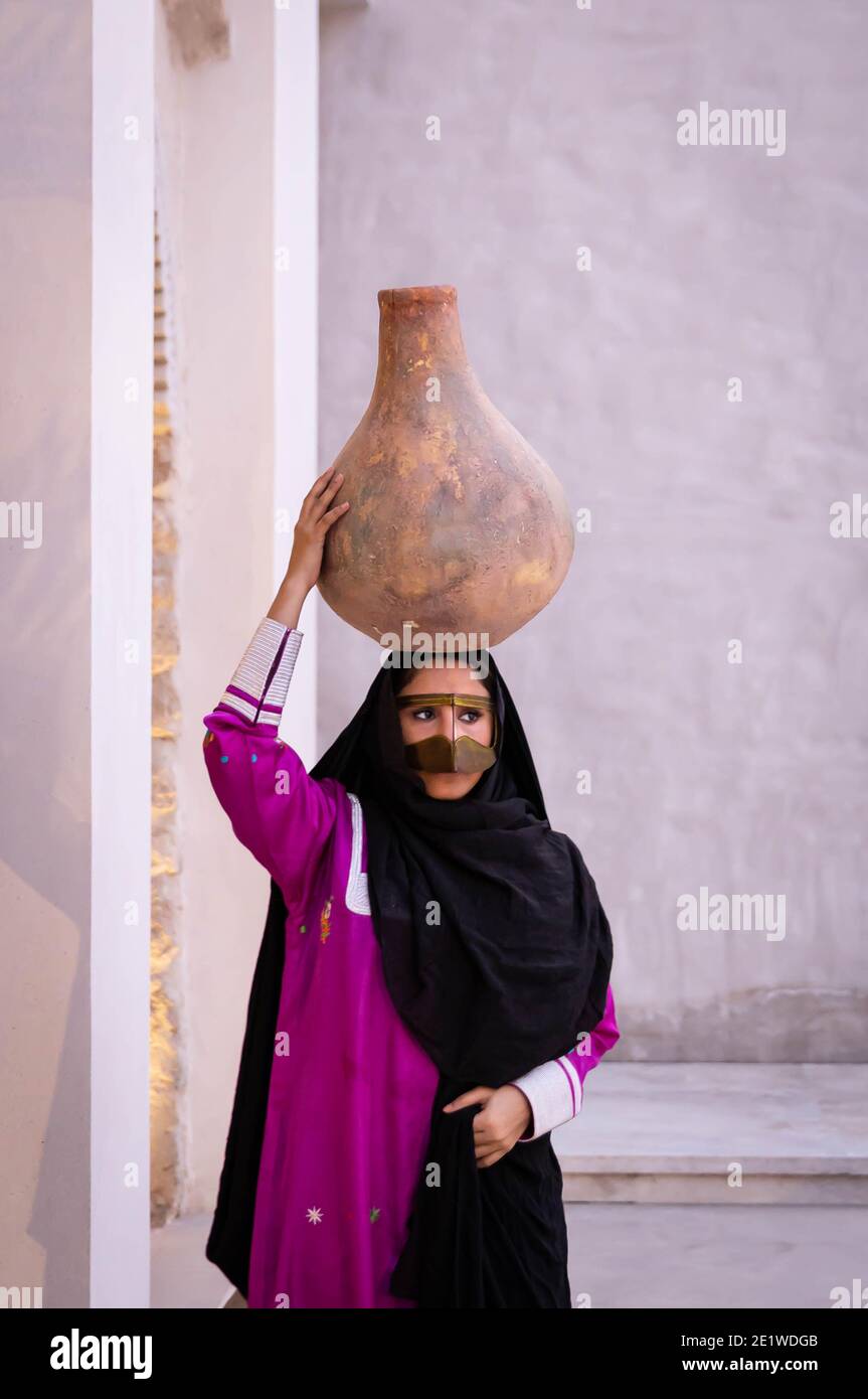 Emarati lady in traditional clothes holding a jar over her head and roaming around the house Stock Photo