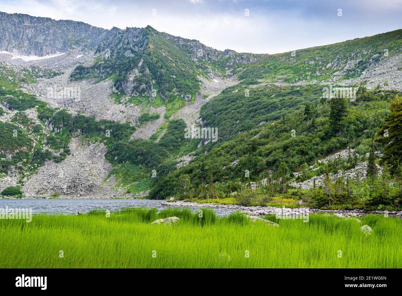 Lake at foot of mountain range. River in mountain valley along rocks. Summer morning in mountains of Siberia Stock Photo