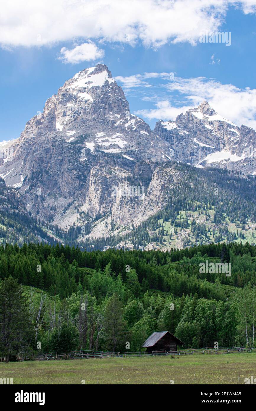 Small log cabin sits in peaceful meadow in the shadow of jagged mountain peaks of Grand Teton National Park Stock Photo