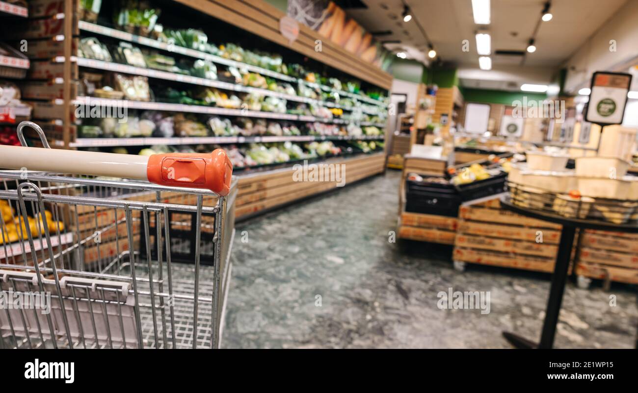 Empty shopping cart in supermarket. Food products on shelves in grocery store. Stock Photo