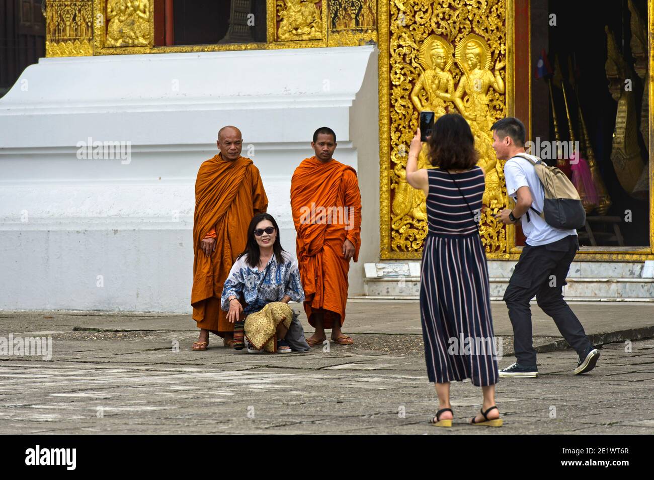 Tourists taking selfies with monks at the entrance to the House of the Royal Funeral Chariot, Wat Xieng Thong Temple, Luang Prabang, Lao Stock Photo