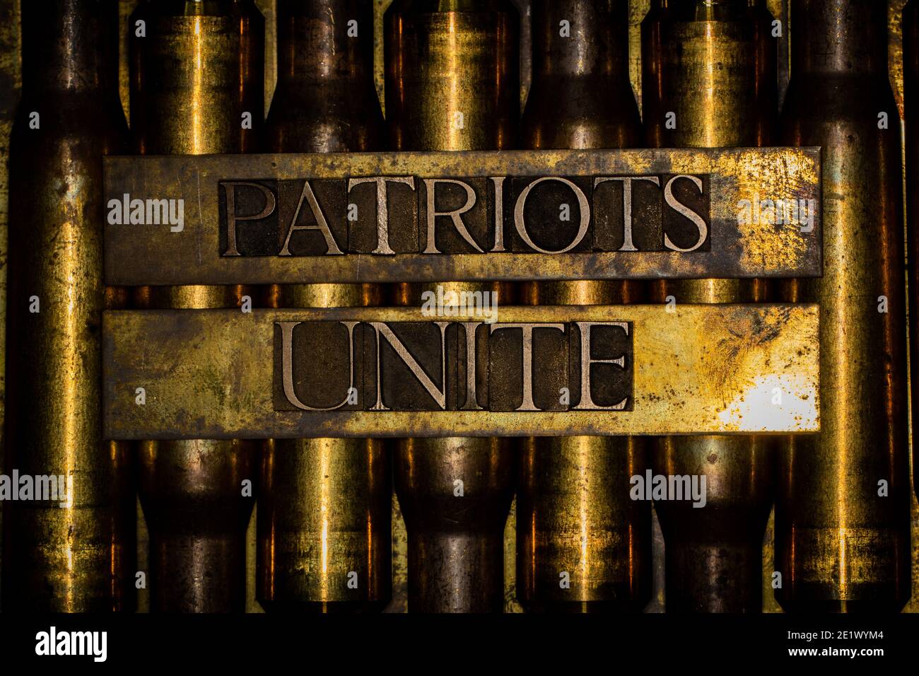 Patriots Unite text over copper 50 caliber bullet casings surrounded by barbed wire on grunge background Stock Photo
