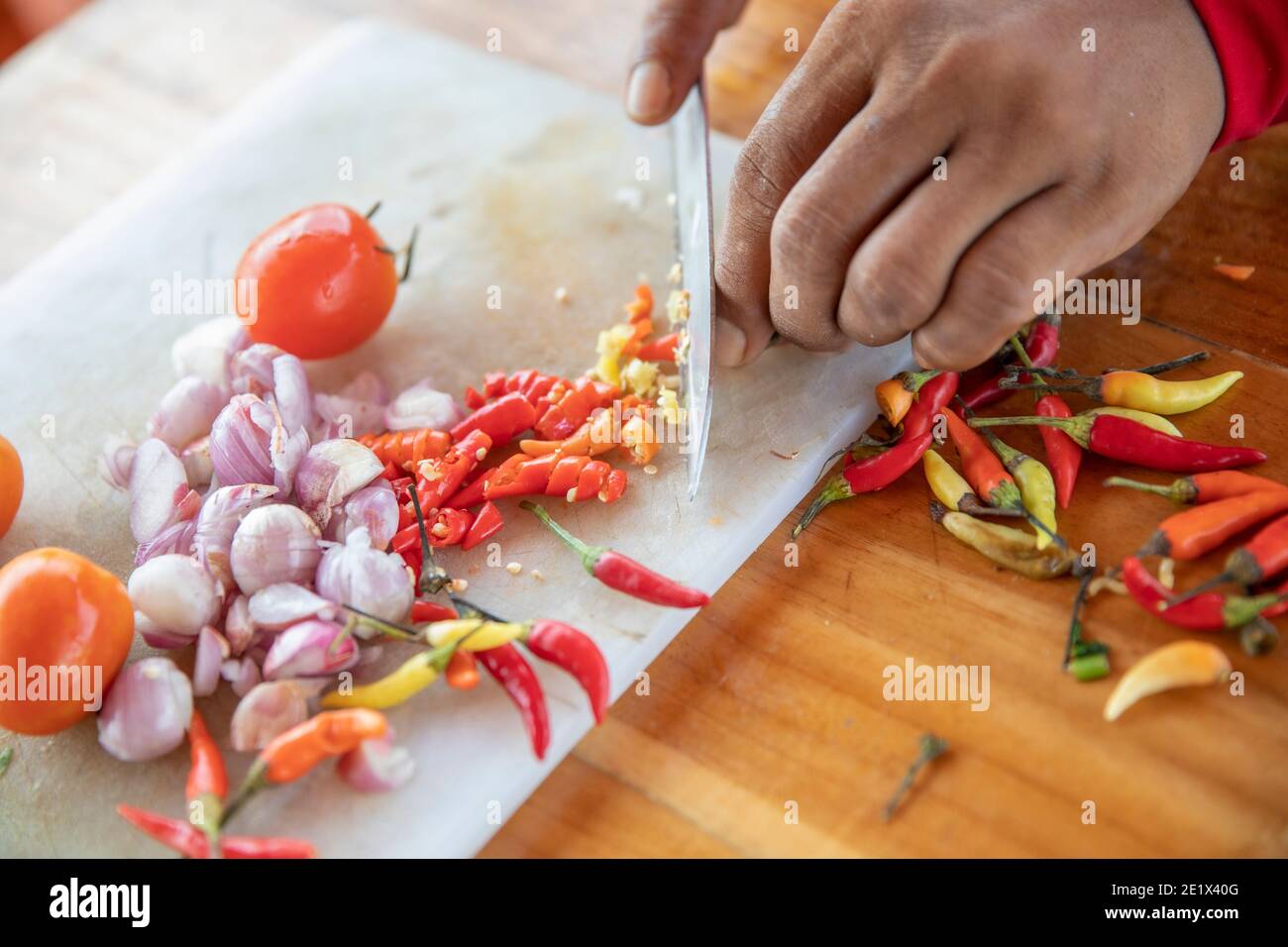 close up of a hand cutting white onions and chilli pepper on a kitchen board with a knife Stock Photo