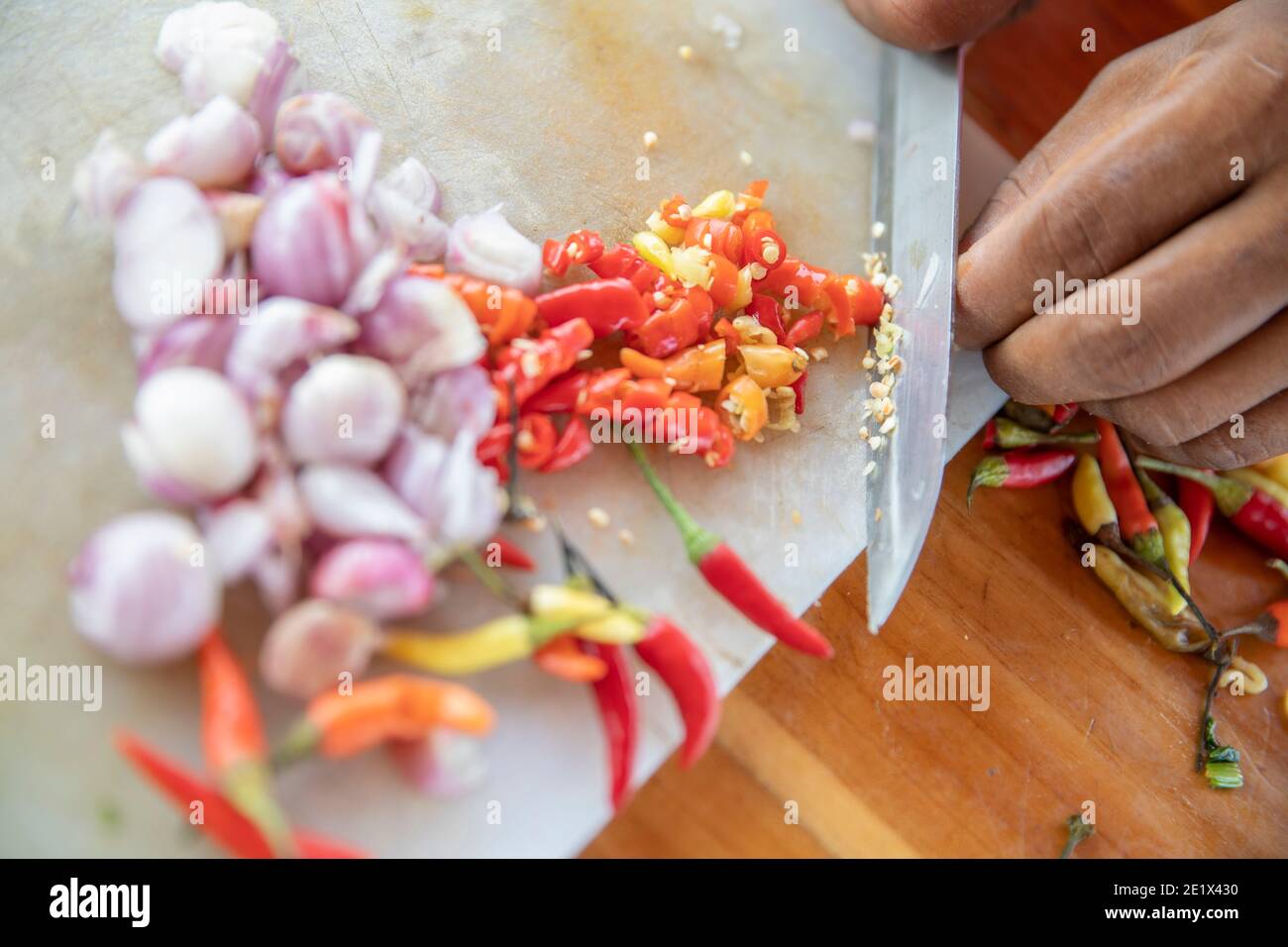 close up of a hand cutting white onions and chilli pepper on a kitchen board with a knife Stock Photo